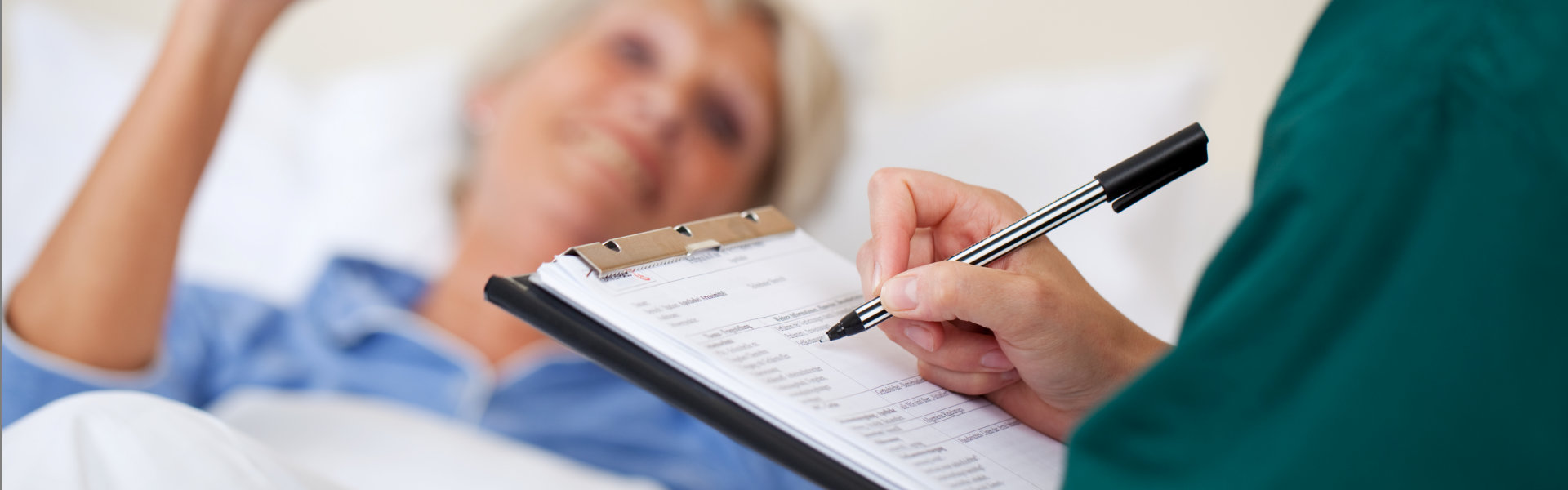 nurse writing on clipboard while looking at patient